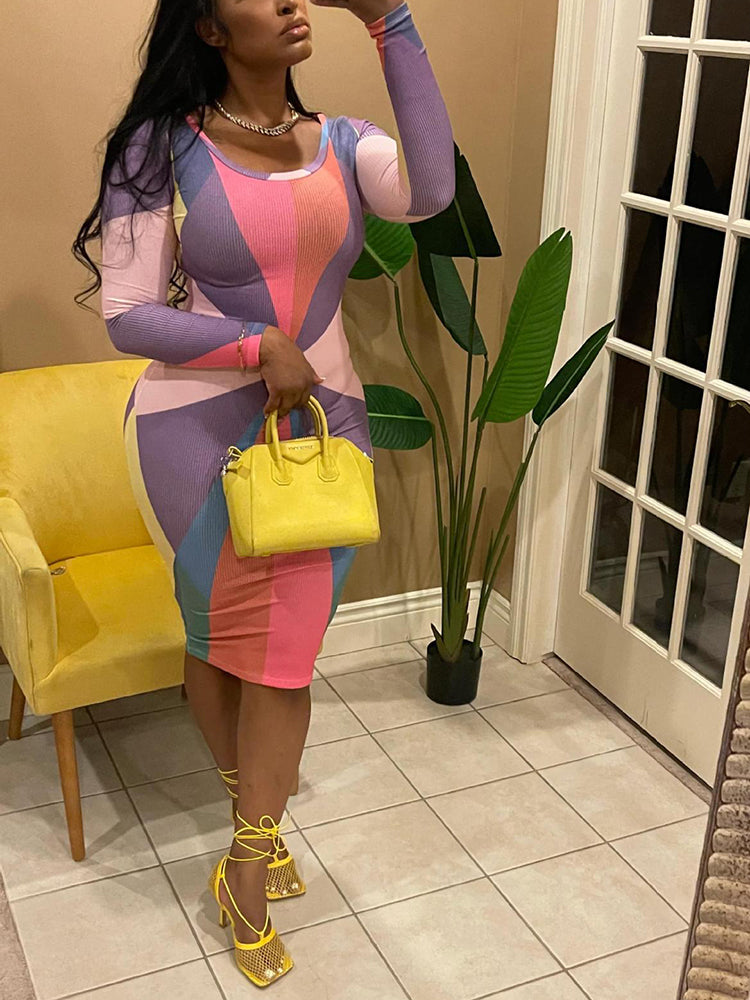 Woman in a long-sleeved, multi-colored geometric print bodycon dress and yellow strappy heels, posing for a mirror selfie.