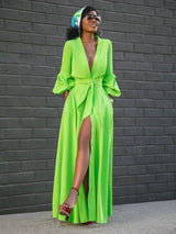 A woman models a flowing lime green maxi dress with long puff sleeves and a dramatic high slit, styled with a headscarf and elegant jewelry.