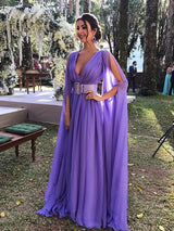 Woman in a long purple formal dress with cape sleeves and a white belt, standing outdoors