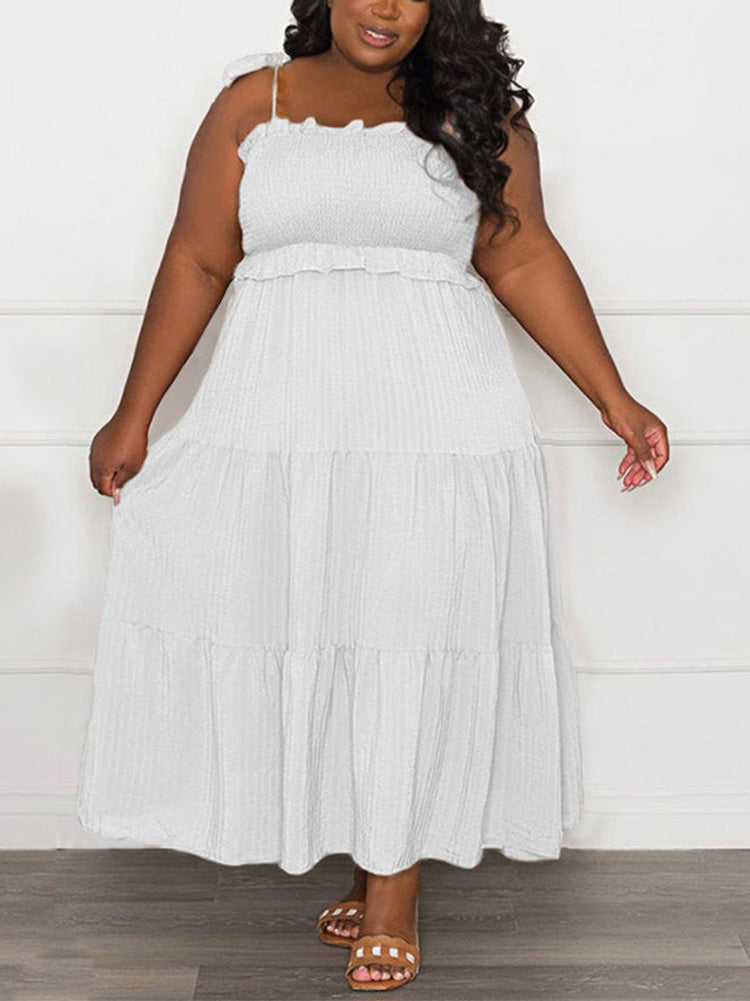Plus-size woman wearing a white tiered maxi dress with tie shoulder straps and a smocked bodice, standing indoors.