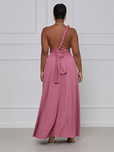 Back view of a woman wearing a dusty rose maxi dress styled as a one-shoulder with a tie detail.