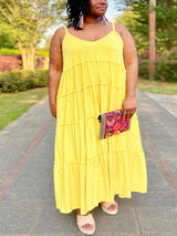 Woman wearing a yellow tiered maxi dress with spaghetti straps and a v-neckline, holding a colorful clutch.