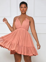 Close-up of a woman in a coral pink halter neck mini dress with a deep V-neckline and tiered ruffled skirt, her arm extended.