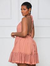 Rear view of a woman wearing a coral pink halter neck mini dress with an open back and tie detail, showing the tiered ruffled skirt.
