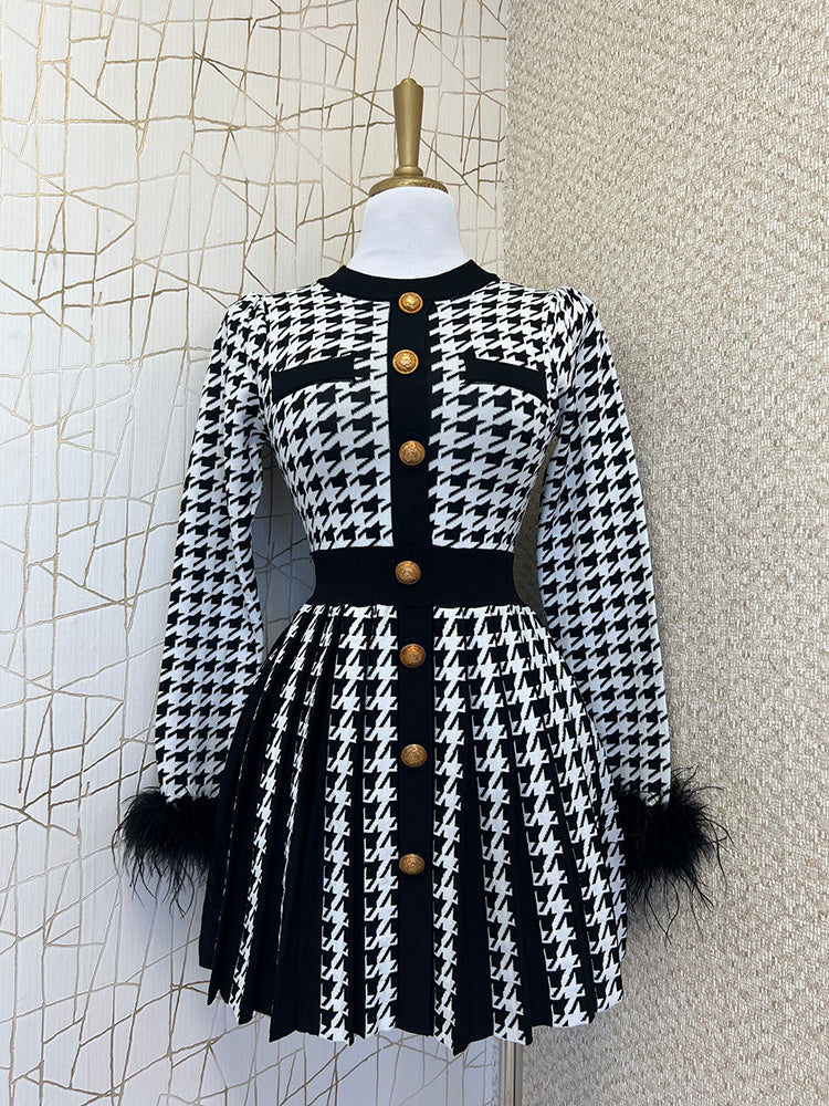Black and white houndstooth knit dress with feather trim cuffs and a pleated skirt displayed on a mannequin.