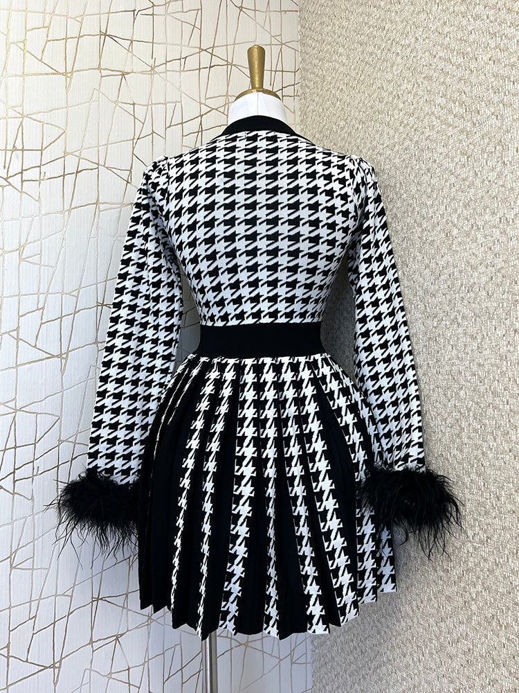 Back view of a black and white houndstooth knit dress with feather trim cuffs and a pleated skirt on a mannequin.