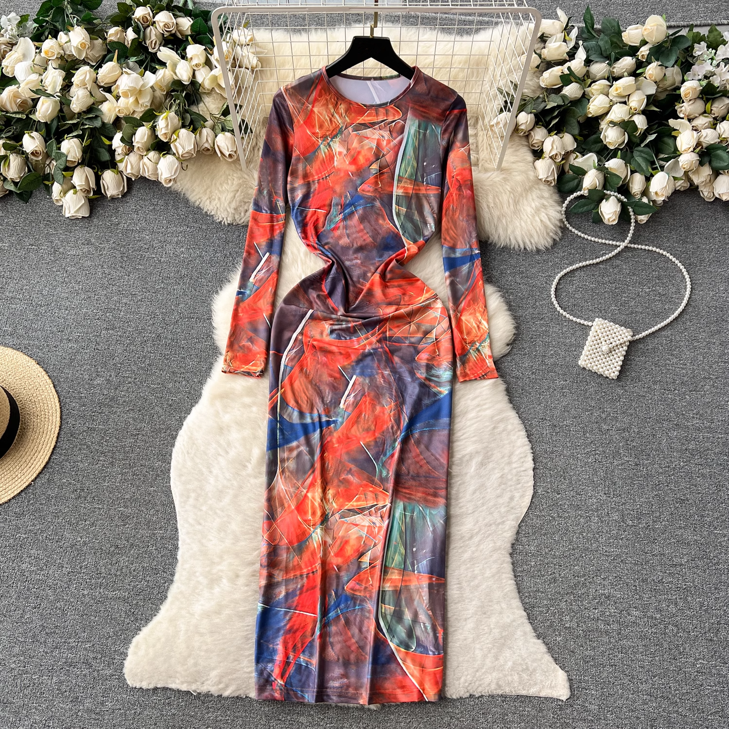 A long-sleeved, abstract print maxi dress with a side slit is laid flat on a white faux fur rug.