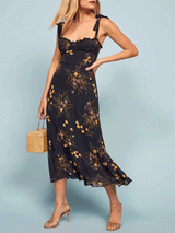 Woman wearing a black floral print midi dress with tie shoulder straps and a ruffled neckline.