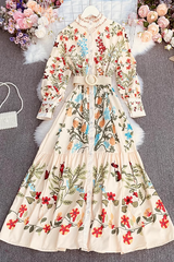 Cream floral print maxi dress with long sleeves and a belted waist, laid flat on a grey background with decorative flowers and accessories.