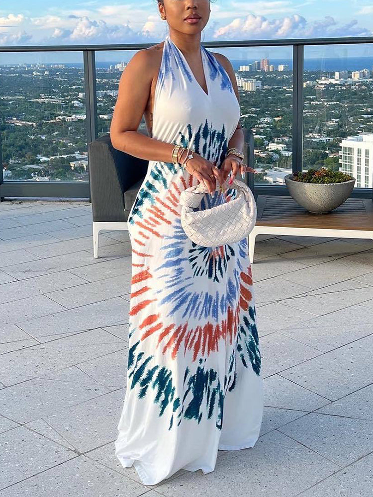 Woman wearing a white maxi dress with a colorful tie-dye print on a balcony overlooking a city skyline.