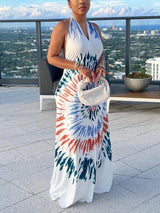 Woman wearing a white maxi dress with a colorful tie-dye print on a balcony overlooking a city skyline.