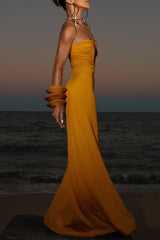 Side profile of a woman in a yellow floor-length gown with a deep V-neckline and ruched detailing, on a beach.
