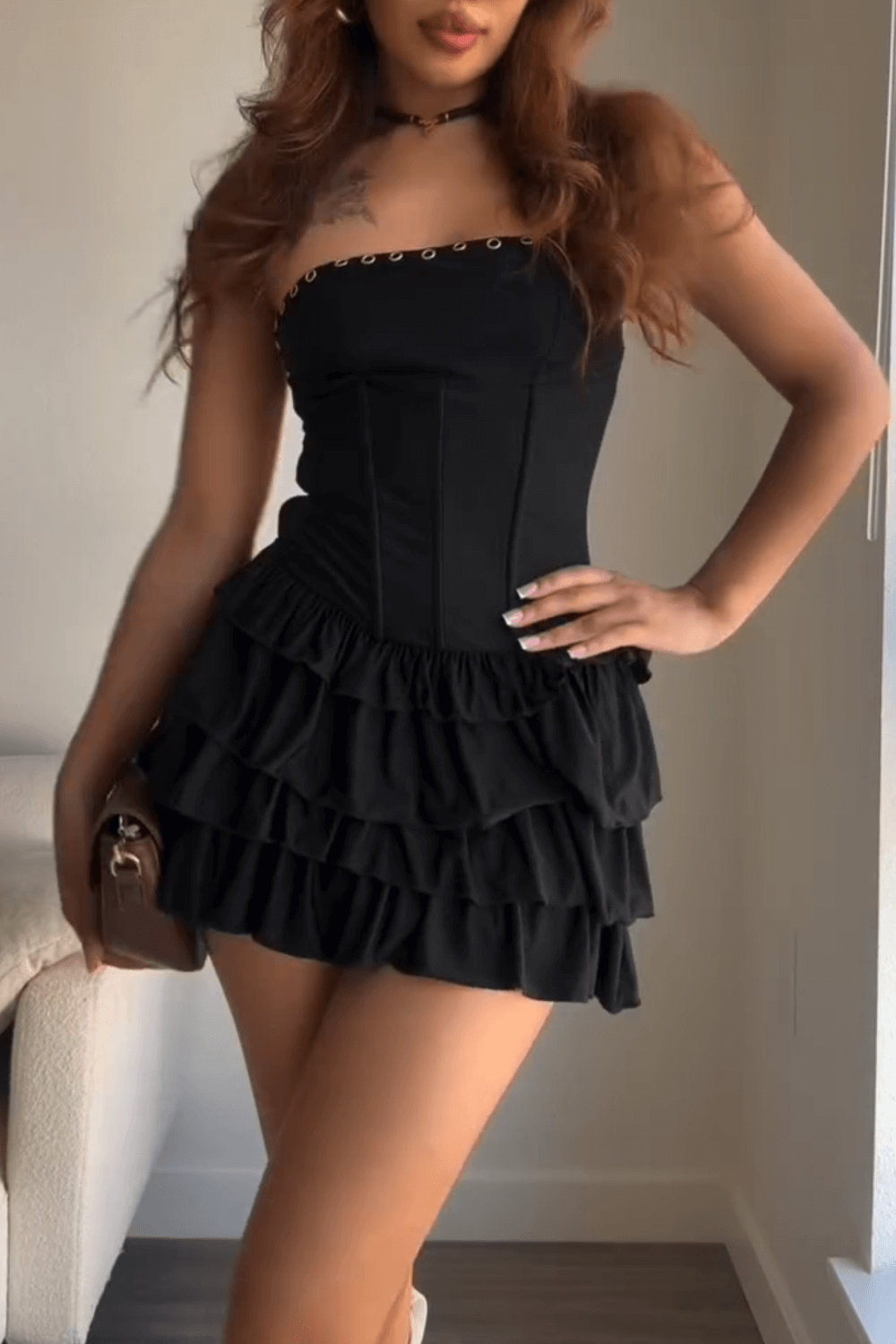 Woman wearing a black strapless mini dress with a ruffled skirt and corset bodice.