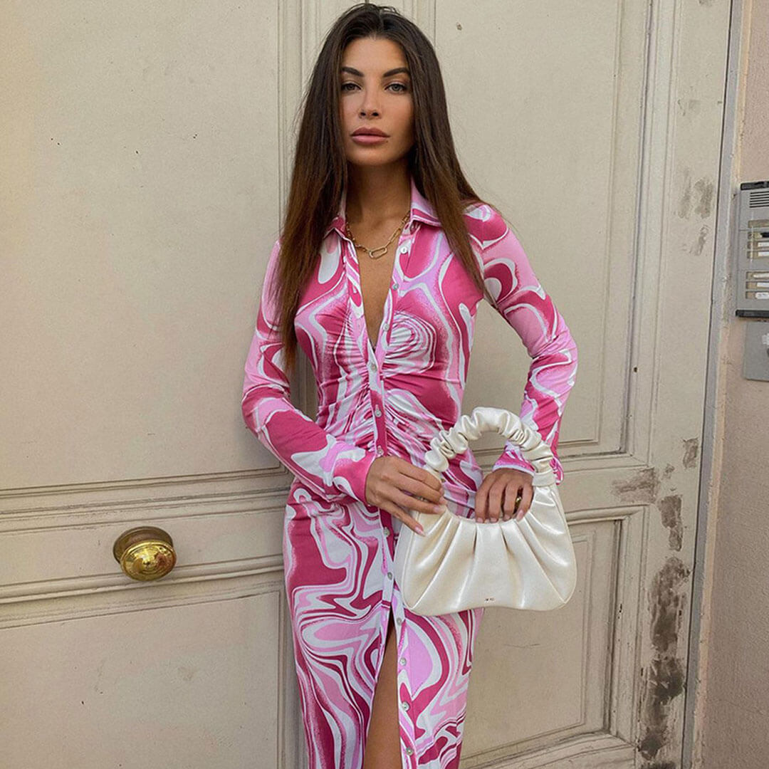 Front view of a woman in a pink and white abstract print bodycon midi dress, holding a white ruched handbag.