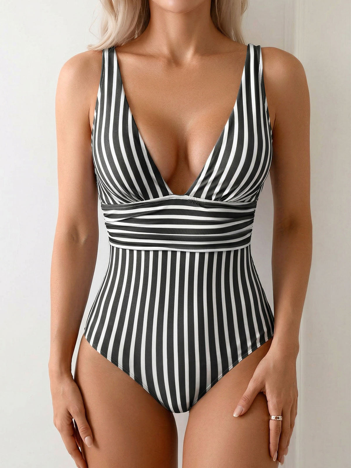 Woman wearing a black and white striped one-piece swimsuit with a deep V-neckline and ruched waist detail.