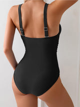 Back view of a woman wearing a black one-piece swimsuit with adjustable straps.