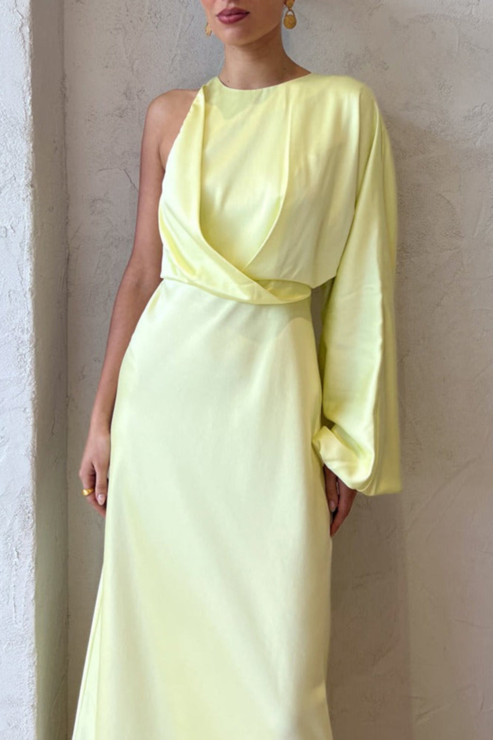 Close-up of the draped bodice and asymmetrical sleeve of a pale yellow satin one-shoulder maxi dress on a model.