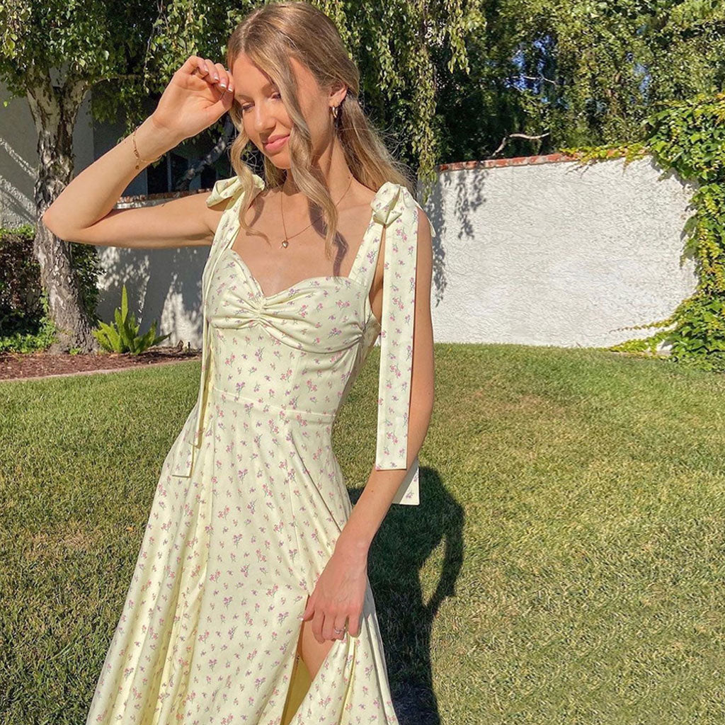 Close-up of a woman wearing a yellow floral print midi dress with tie shoulder straps and a sweetheart neckline, posing in a garden.