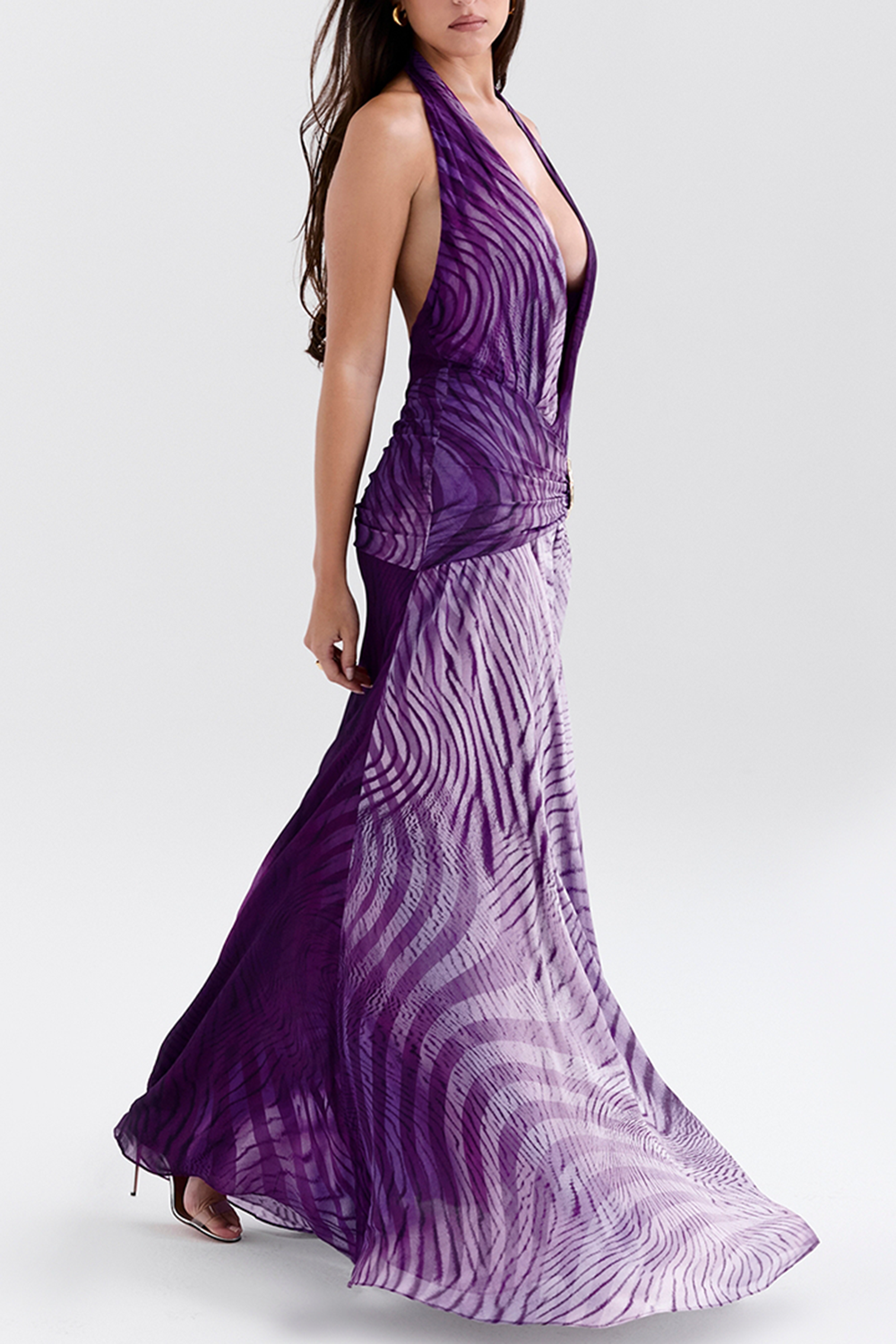 Woman walking in a purple halter neck maxi dress with a dramatic draped skirt and print.