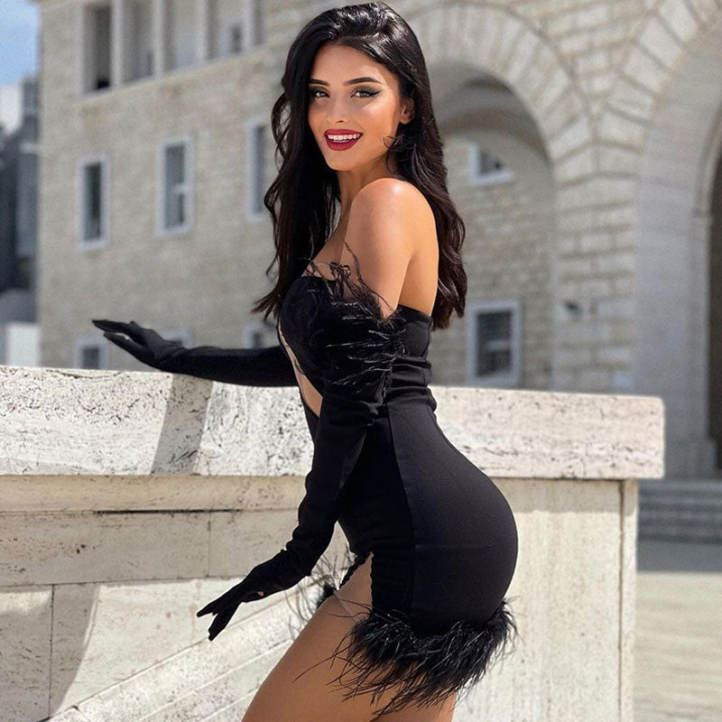 Woman in a black feather-trimmed dress with cut-out detail and long sleeves, smiling.