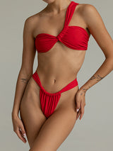 Woman wearing a red one-shoulder bikini with twisted bust and high-cut bottoms.