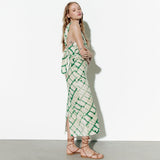 Side view of a woman in a green and cream tie-dye column dress with an asymmetrical halter neckline and a back tie detail.