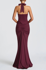 Back view of a woman wearing a burgundy floor-length halter dress with a deep V-neckline and ruched detailing.