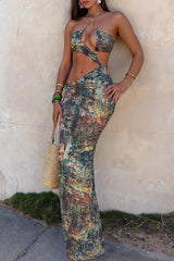 Woman in a patterned halter maxi dress with side cut-outs, leaning against a wall.