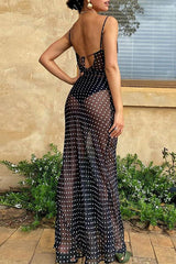 Rear view of a woman wearing a black polka dot sheer maxi dress with spaghetti straps and a cowl neck.