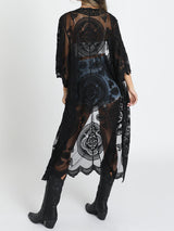 Back view of a woman wearing a black lace kimono over a white crop top and denim shorts