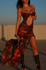 woman wearing a tie-dye print maxi dress with a high slit and cut-out, posing outdoors at sunset with boots