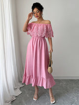 Woman wearing a pink off-the-shoulder maxi dress with lace bodice and ruffled hem, holding a straw bag, front view