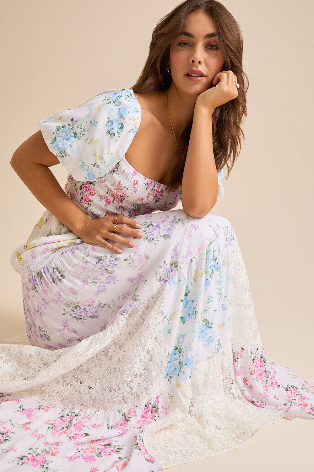 Woman wearing a white floral print maxi dress with puff sleeves and a square neckline, kneeling and posing.