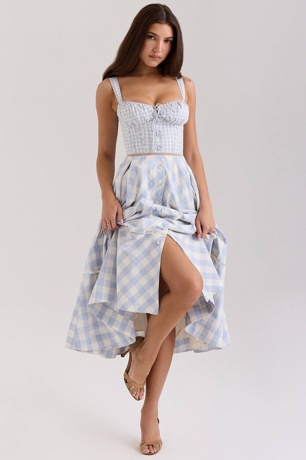 Woman lifting the skirt of a blue and white gingham check midi dress, revealing a slit.