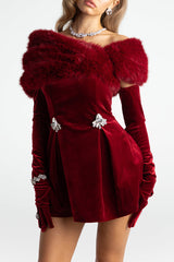 Model wearing a red velvet off-the-shoulder mini dress with feather trim and long gloves.