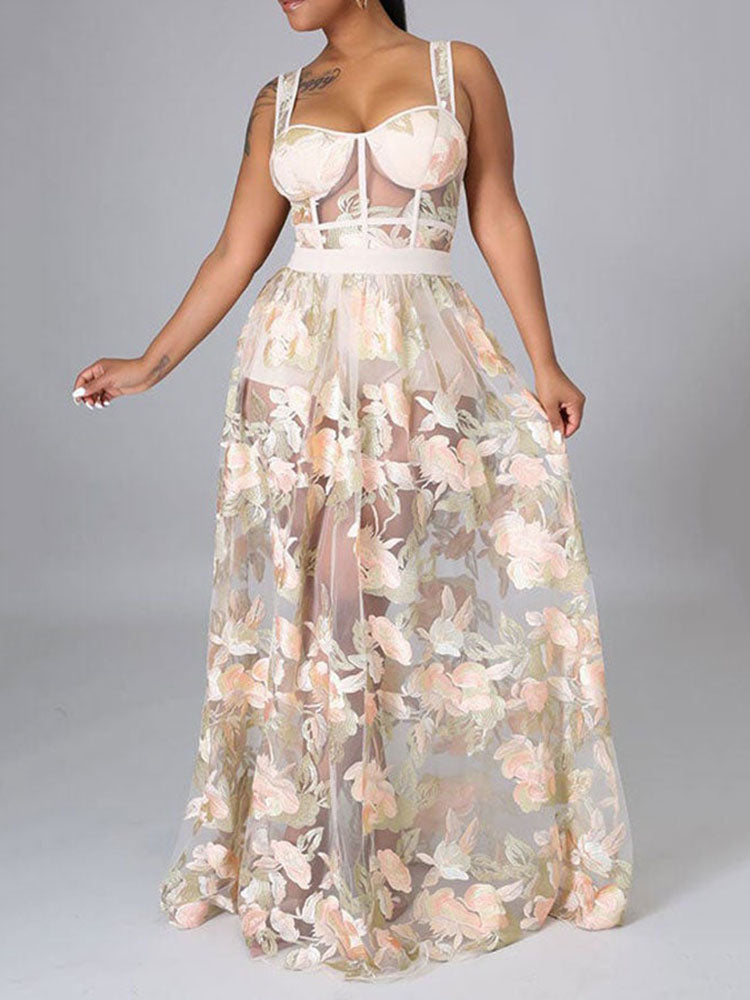 Woman in a sheer floral embroidered maxi dress with a corset-style bodice, posing against a grey background.