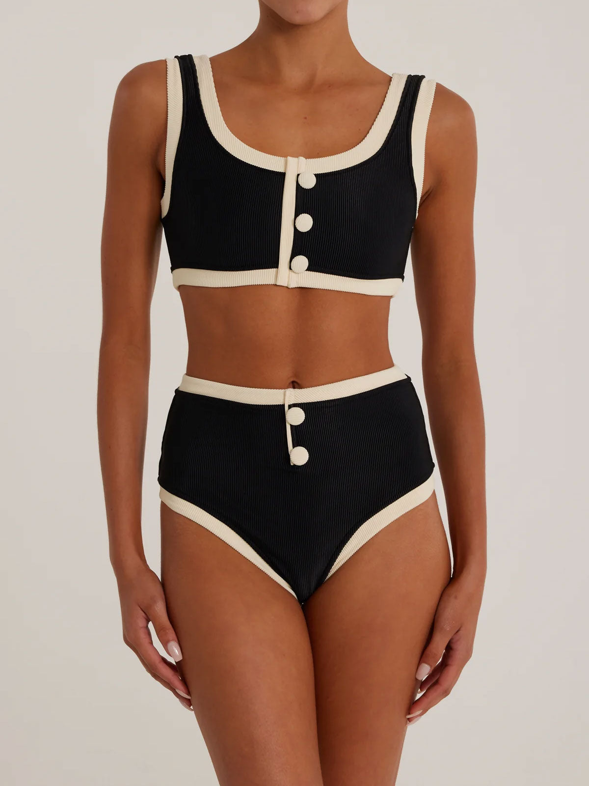 Woman wearing a black and cream ribbed bikini set, front view.