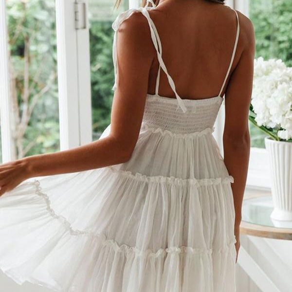 Back view of a woman in a white tiered mini dress with a smocked bodice and tie shoulder straps.