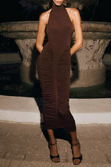 Woman wearing a brown ruched halter dress with a backless design, standing in front of a fountain.