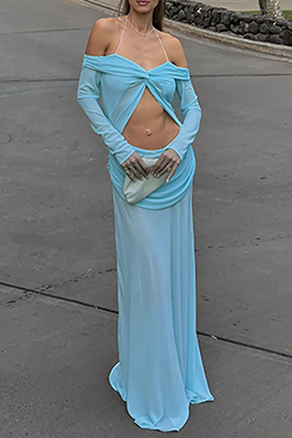 Full-body shot of a woman in a light blue flowing gown with a cut-out at the waist, standing on a paved surface.