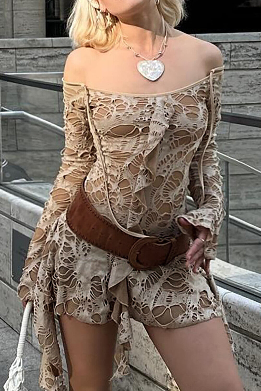A woman models a beige distressed off-the-shoulder dress with a brown belt and snakeskin boots.