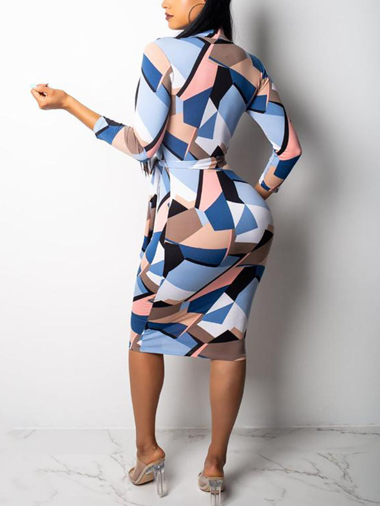 Rear view of a woman wearing a long-sleeved geometric print pencil dress with a belted waist and V-neckline, standing against a white background.