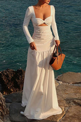 Woman wearing a white long sleeve maxi dress with a cutout and sweetheart neckline, standing by the sea.