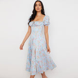 Side view of a woman in a light blue floral midi dress with a thigh-high slit and puff sleeves.