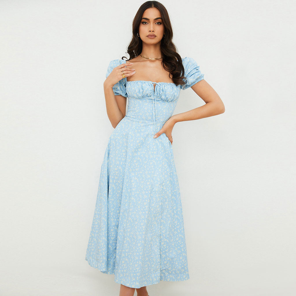 Woman wearing a light blue floral print midi dress with puff sleeves and a square neckline, standing against a white background.