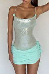 Woman posing in a light blue sequined mini dress with ruched skirt and floral accents, showing one arm raised