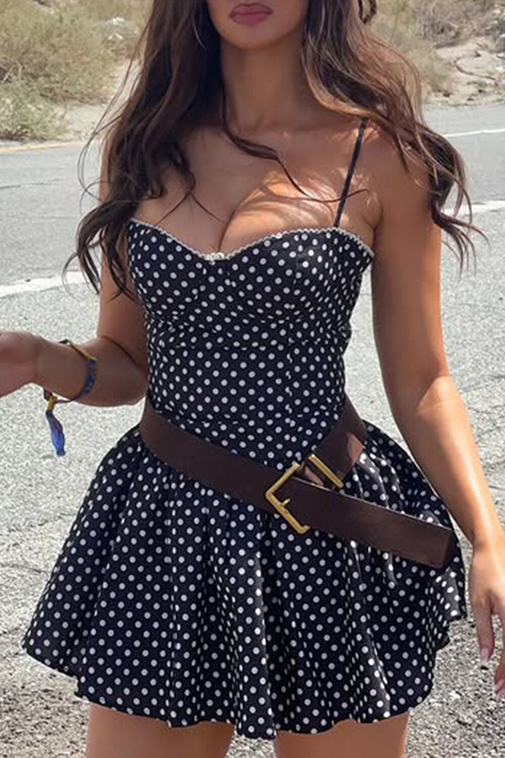 Woman wearing a black and white polka dot mini dress with a brown belt and cowboy boots.