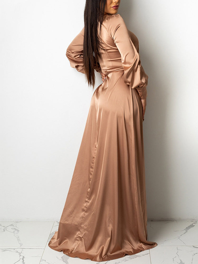 Rear view of a woman in a champagne satin wrap maxi dress with a high slit and long puff sleeves.