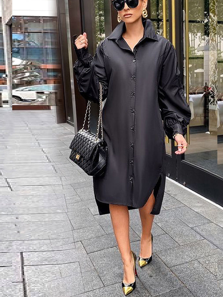 Woman wearing a black collared shirt dress with long ruffled sleeves and an asymmetrical hemline, carrying a black handbag and wearing black and gold heels.