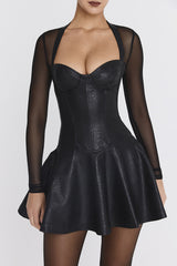 Studio shot of a woman wearing a black faux leather mini dress with sheer long sleeves and a halter neckline.